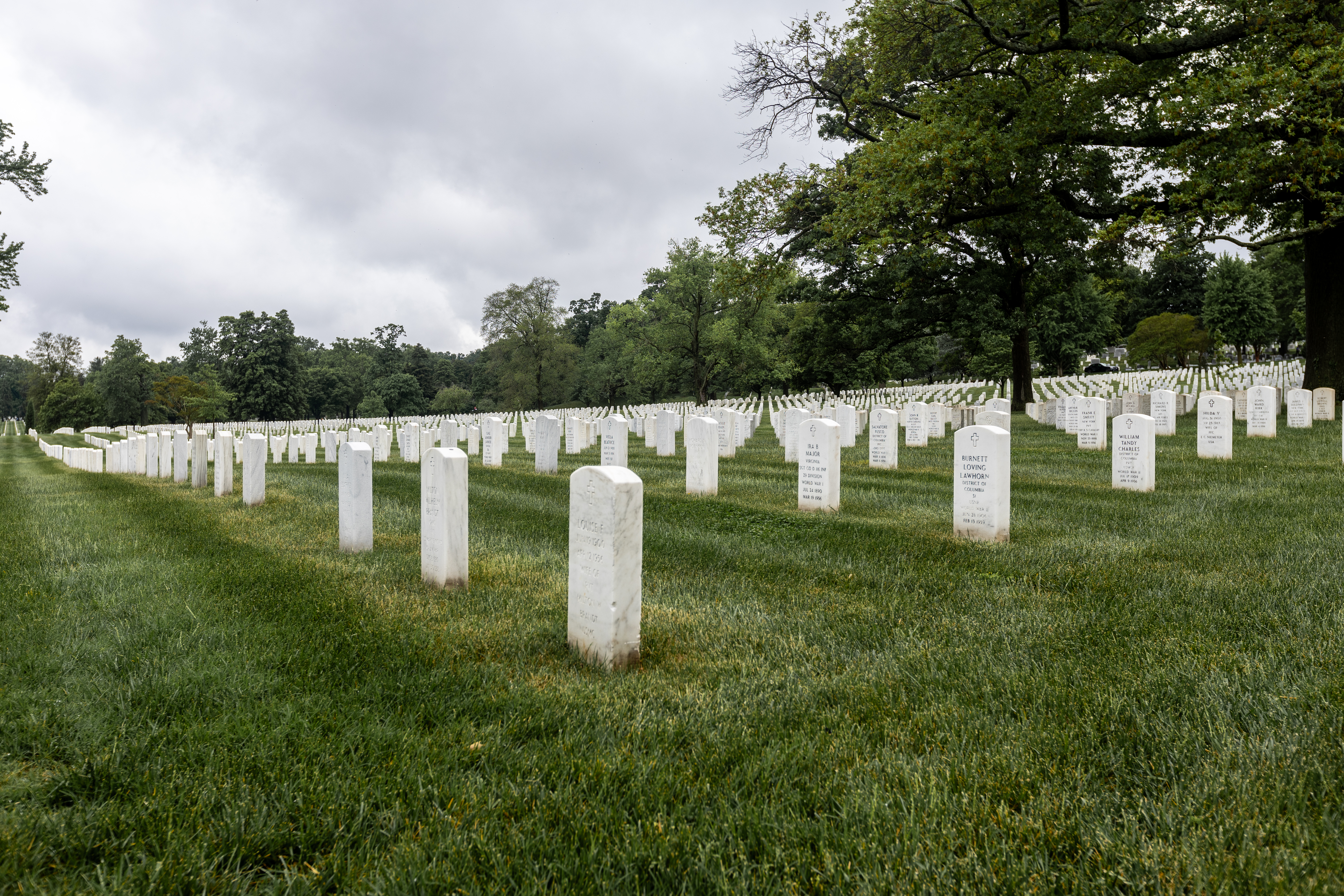 Rows of white marble headstones on a green lawn at a national cemetery